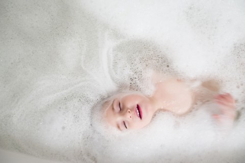 Girl (2-3) lying in bathtub