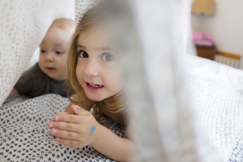 Girl (2-3) and baby brother (6-11 months) hiding under bed covers