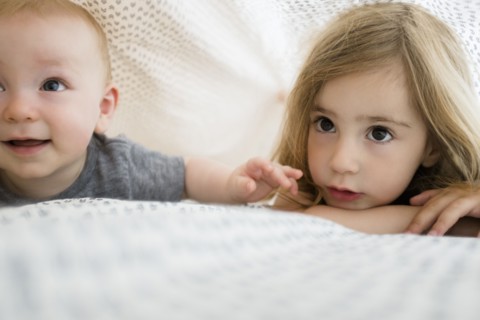 Girl (2-3) and baby brother (6-11 months) hiding under bed covers