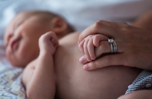 Mother holding son's (0-1 months) hand in bedroom