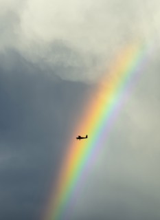 Silhouette of small plane flying through rainbow