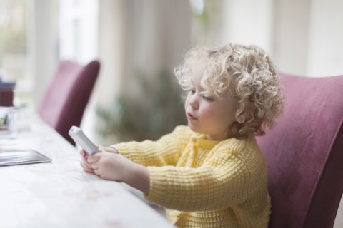 Blond girl (4-5) sitting at table and looking at mobile phone