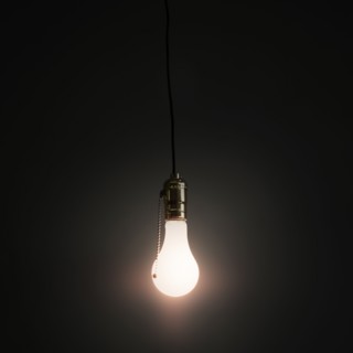 Light bulb hanging against grey background.
