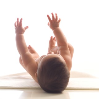 Naked baby girl (6-11 months) lying on back and reaching up.
