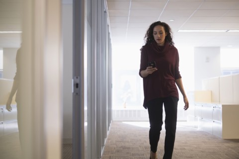 Young woman walking in corridor with mobile phone.