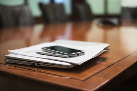 Empty conference table with mobile devices and documents.