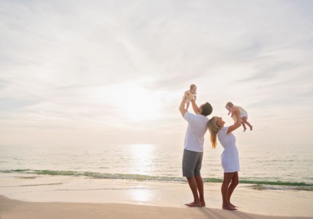 Happy family with two baby girls (2-5 months) at beach in sunlight