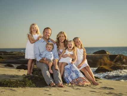 Family with children (12-17 months, 4-5, 6-7, 8-9) sitting on beach with sea in background