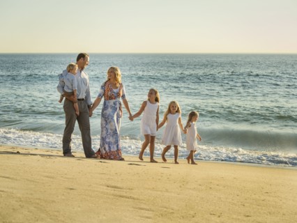 Family with children (12-17 months, 4-5, 6-7, 8-9) walking on beach with sea in background