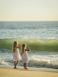 Girls (4-5, 6-7) standing on beach and looking at sea