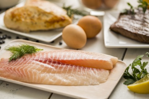 Raw tilapia fish on plate, chicken and eggs in background