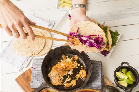 Woman preparing tortilla with tilapia and red cabbage