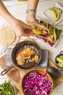 Woman preparing tortilla with tilapia, avocado and red cabbage