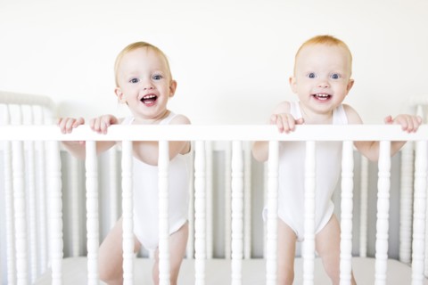 Twin brothers (12-17 months) standing in crib