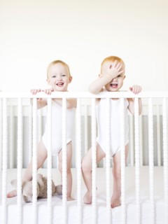 Twin brothers (12-17 months) standing in crib