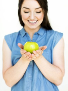 Woman wearing blue top holding green apple