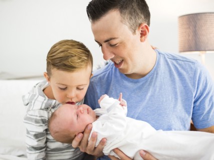 Father carrying daughter (0-1 months) and sitting on bed with son (4-5)