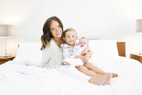 Brother (4-5) carrying sister (0-1 months) and sitting on bed with mother