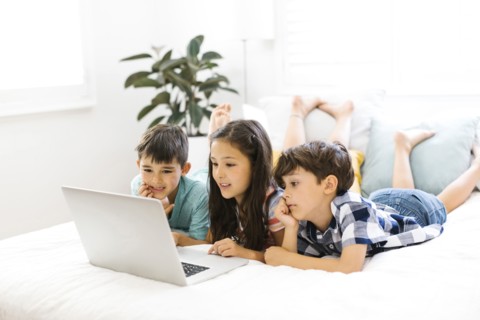 Siblings (10-11, 6-7, 8-9) lying in bed and using computer