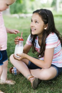 Girl (10-11) sharing bottle of milk with sister (2-3) in park