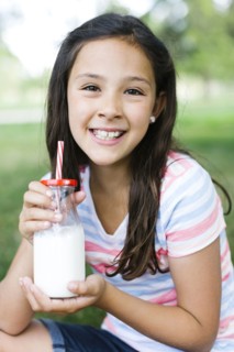 Girl (10-11) in park holding glass of milk with straw