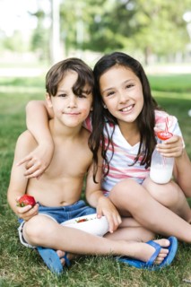 Boy (6-7) and girl (10-11) sitting arm around on grass in summer
