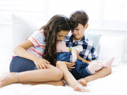 Three siblings (6-11 months, 6-7, 10-11) sitting together on bed
