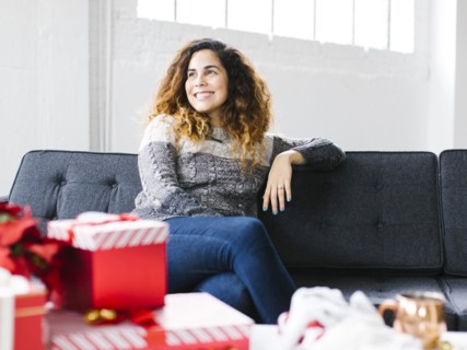 Happy woman on sofa with Christmas gifts in foreground