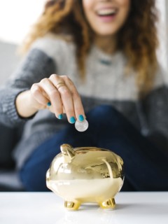 Woman dropping coin into gold piggy bank