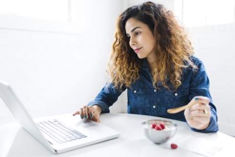 Woman using laptop and eating yoghurt