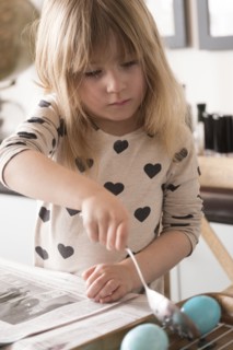 Girl (4-5) making colored Easter eggs