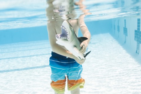 Boy (6-7) playing with toy shark in swimming pool