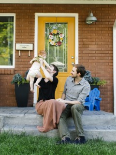 Parents with daughter (12-17 months) sitting in front of house