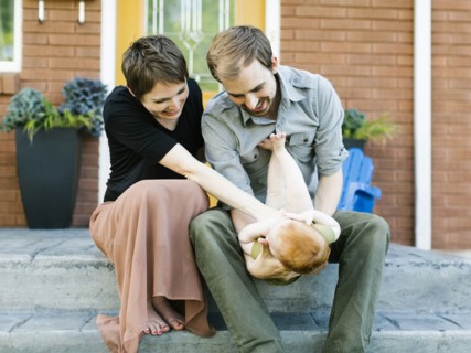 Parents with daughter (12-17 months) sitting in front of house