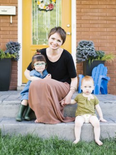 Mother with daughters (2-3, 12-17 months) sitting in front of house