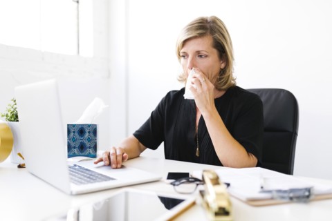 Woman using laptop, blowing nose