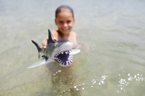 Girl (6-7) playing with toy shark in sea