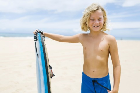Boy (8-9) standing on beach and holding surfboard