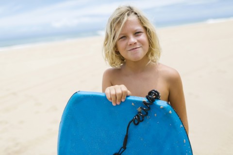 Boy (8-9) standing on beach and holding surfboard