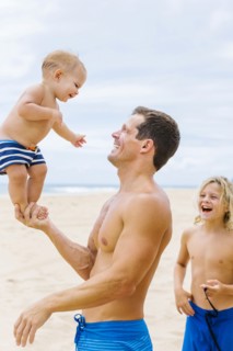Father playing with sons (12-17 months, 8-9) on beach