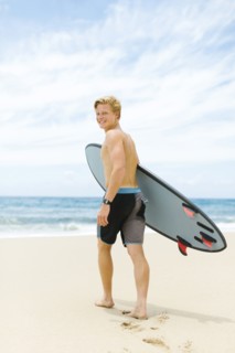 Man walking on beach and holding surfboard