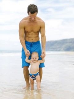Son (12-17 months) learning to walk with father on beach