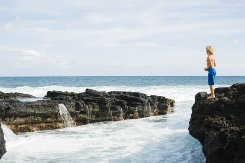 Boy (8-9) standing on rock against blue sky