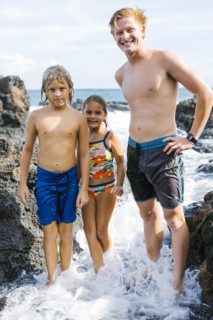Man and children (6-7, 8-9) standing between rock in sea