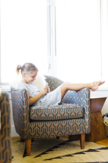 Young girl (6-7) sitting on armchair and using mobile phone