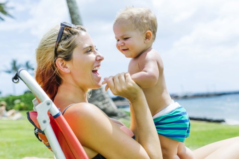 Woman sitting under palm tree with little son (18-23 months)
