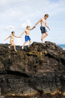 Young man walking on rock with kids (6-7, 8-9)