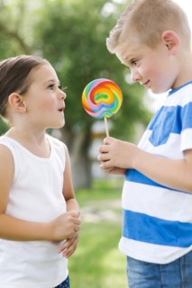 Young boy (6-7) showing sister (4-5) lollipop