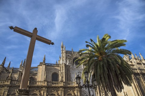Spain, Andalusia, Seville, Cathedral of Seville with palm tree and cross in foreground