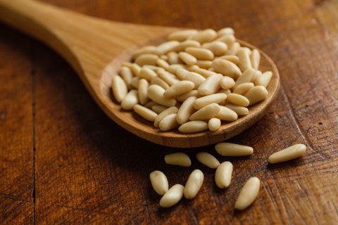 Wooden spoon full of pine nuts on table